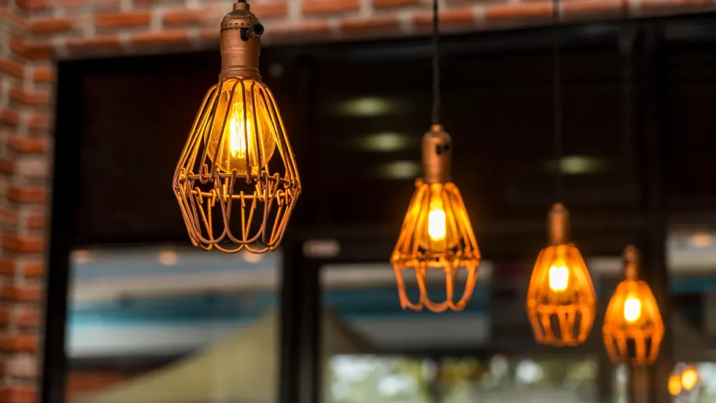 Luminárias pendentes com estrutura metálica e lâmpadas de luz amarelada em ambiente interno com decoração industrial.