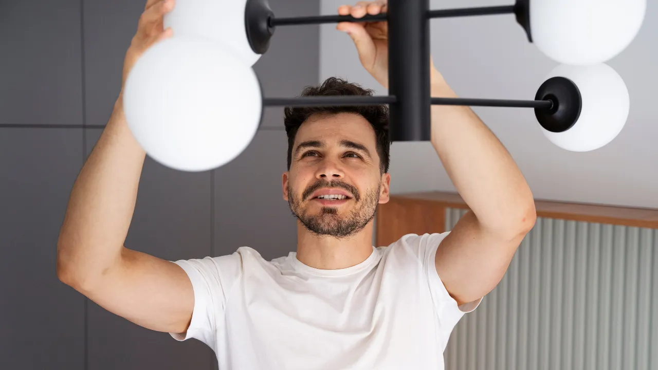 Homem instalando luminária moderna com globos de vidro branco em ambiente interno.