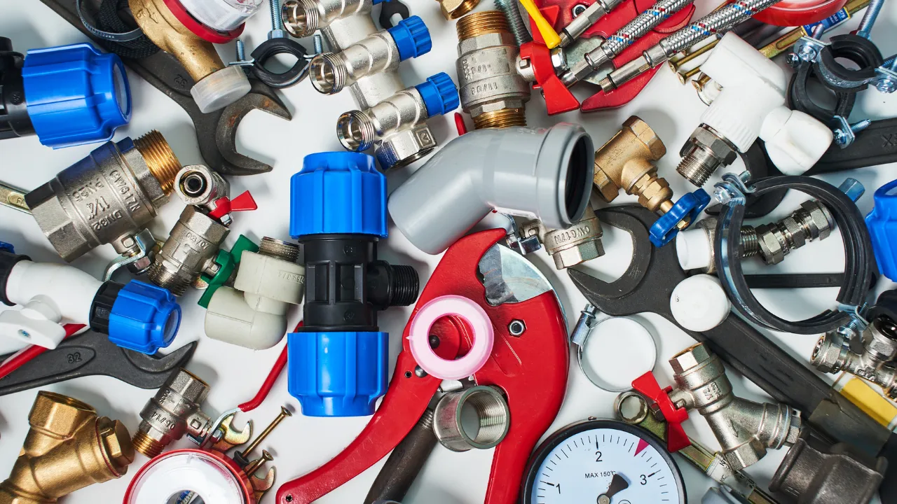 Conjunto de ferramentas e conexões hidráulicas espalhadas sobre uma superfície branca, incluindo chaves, válvulas, canos e medidores de pressão.